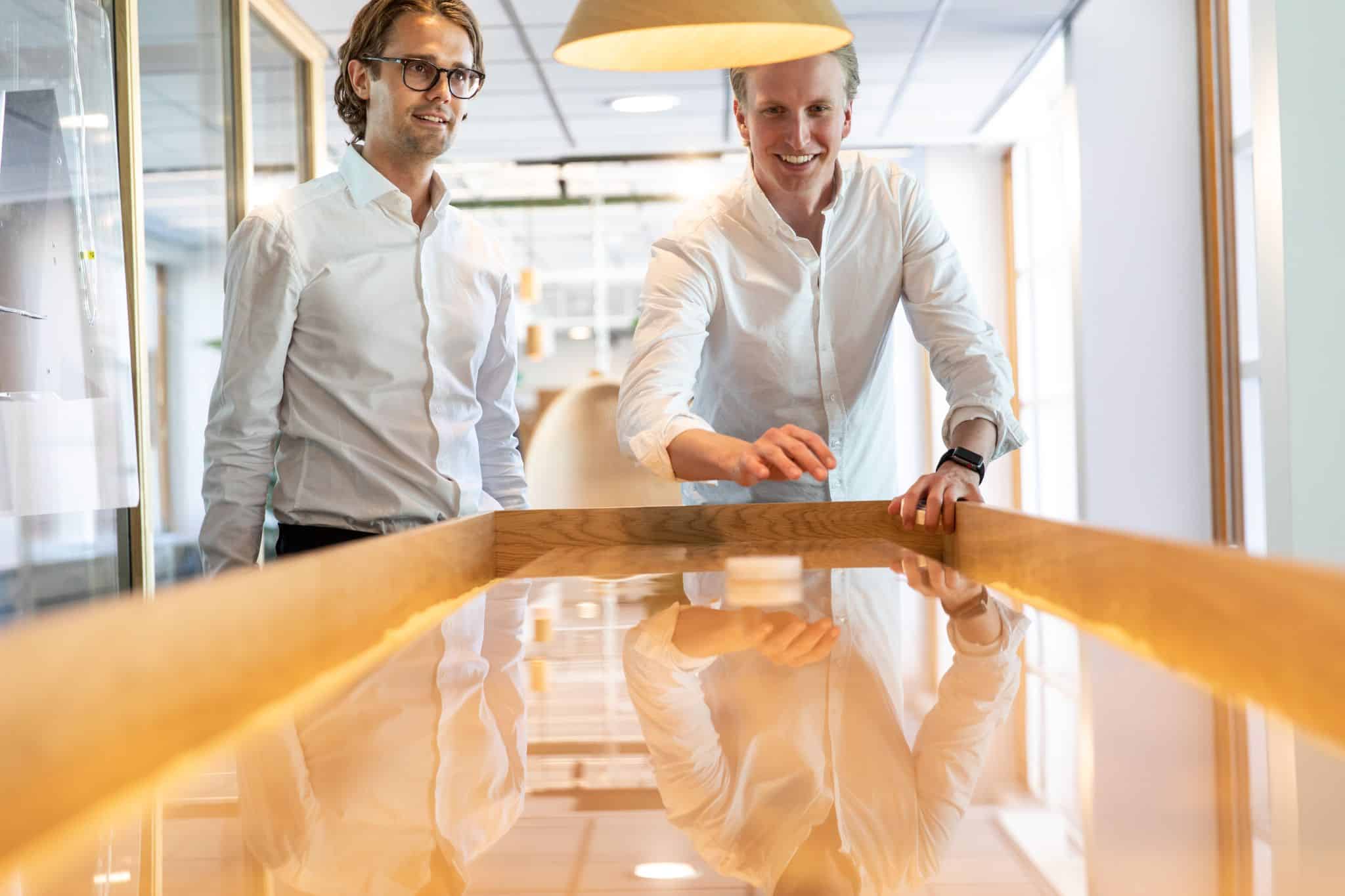Two young professionals in white shirts playing shuffleboard in a bright modern office environment
