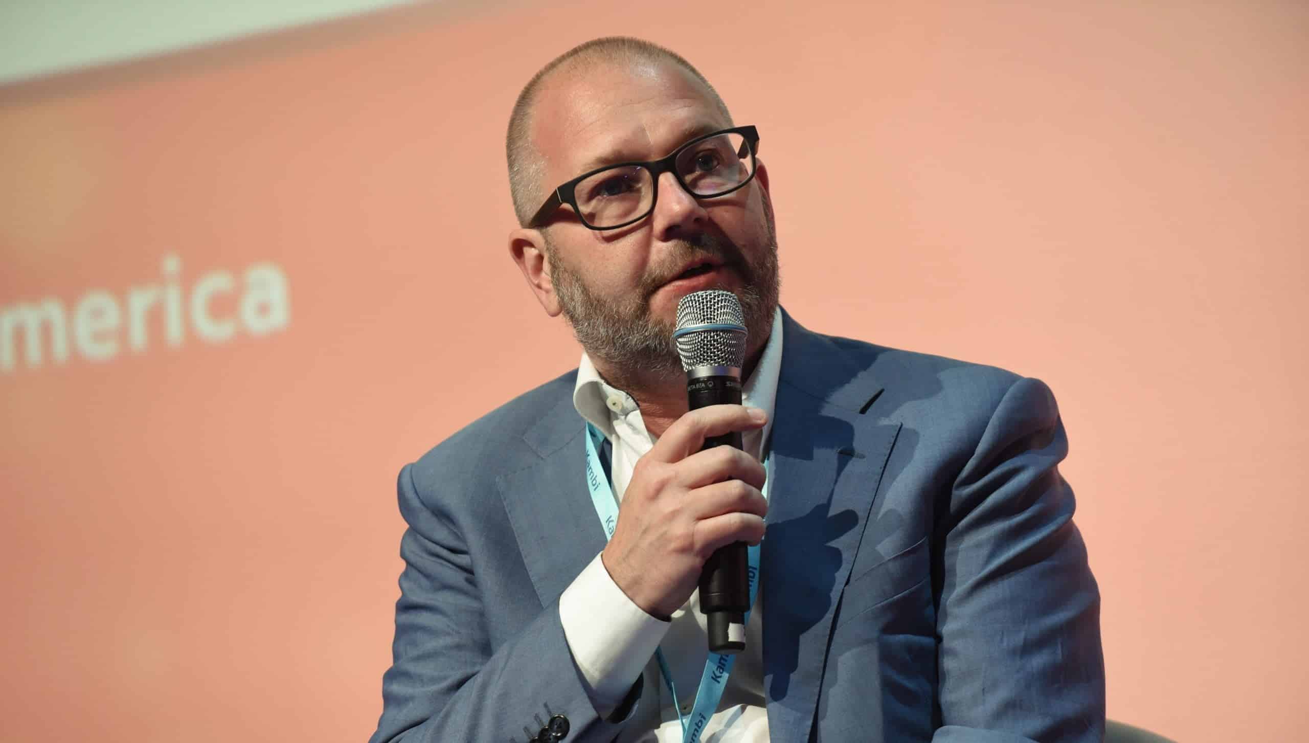 Photo of Kristian Nylén speaking into a microphone at a US conference, with a peach coloured background.