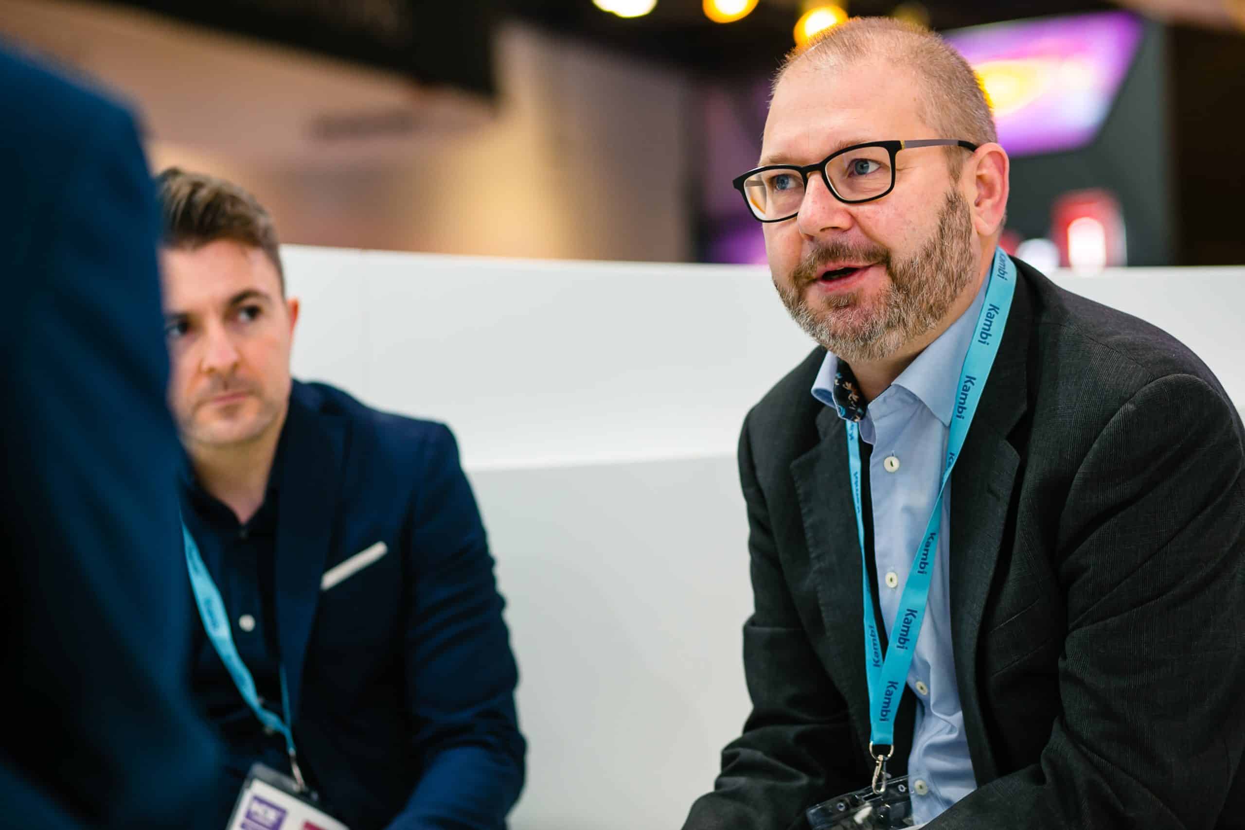 A photo of Kristian Nylén is speaking an individual in business attire engaged in a conversation, seated on a modern couch at a professional event.