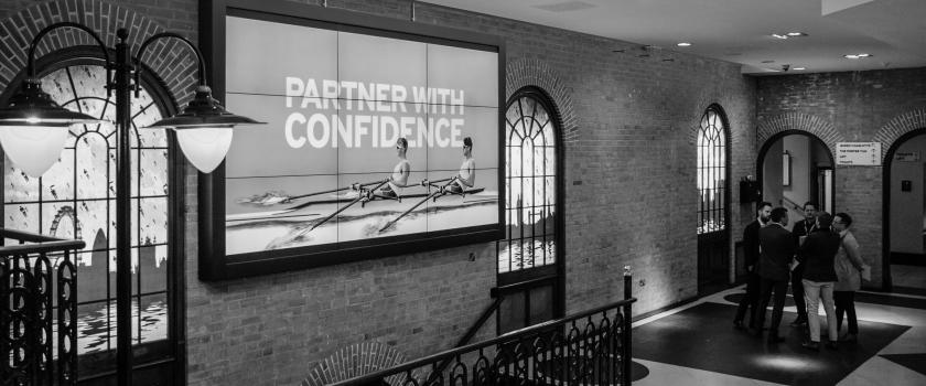 A black and white image of the Kambi office, featuring an picture on the wall of two rowers rowing on water, behind them there are big letters stating 'Partner with confidence'.