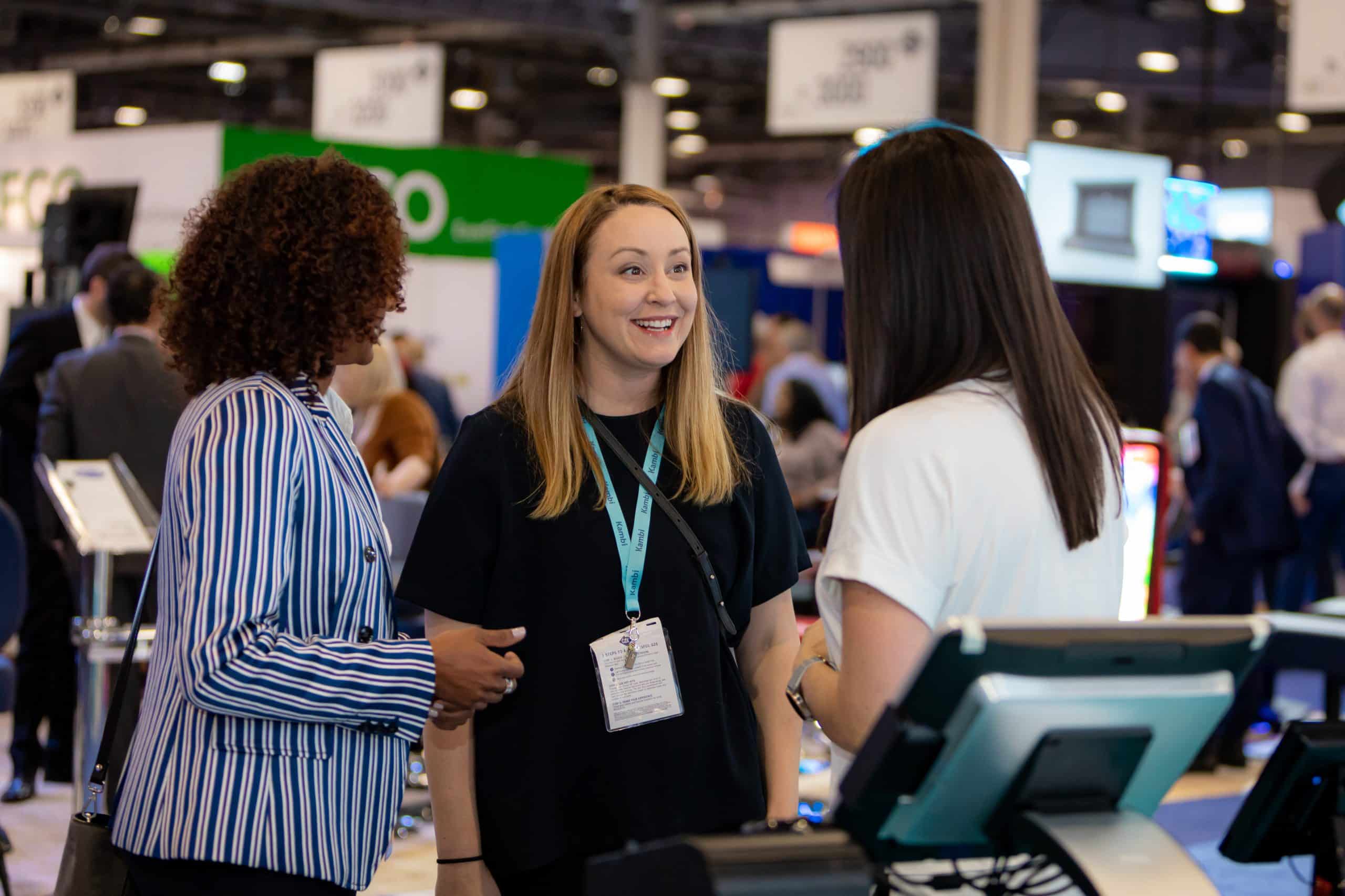 Two women discussing with a Kambi employee during a lively betting event.