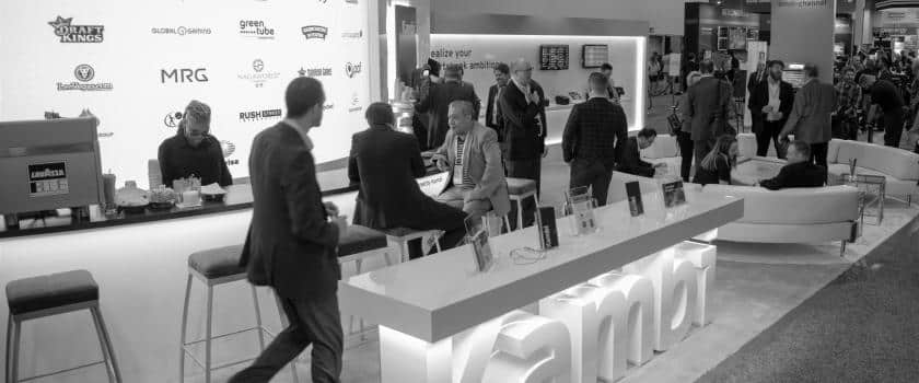Black and white photo of a crowd of people engaged in discussions at a Kambi stand at an event.