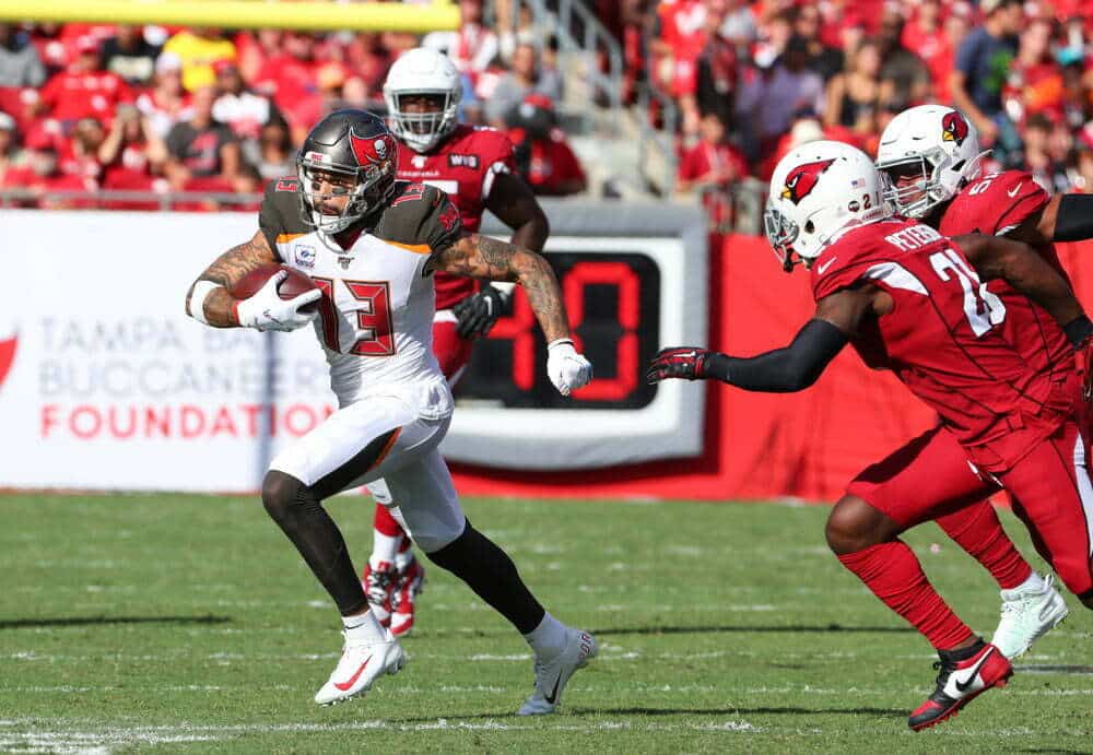 A picture of a four American football players running in a game with fans in the stands behind the players.